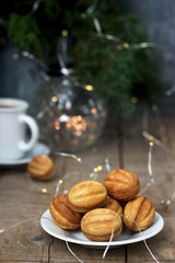Homemade shortbread cookies in the shape of nuts on the background of a cup of coffee, fir branches and garlands.