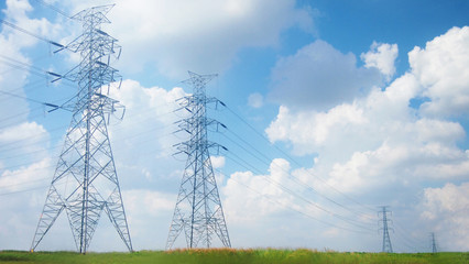 power pylons and high voltage lines with blue sky and green meadow using for electrical...
