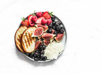 Snack appetizers tapas plate with cheese, figs, olives, berries on a light background, top view