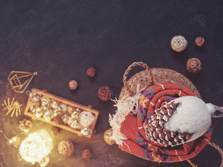 Naklejka premium Christmas composition. Glass balls are in a wooden box. Nearby is a luminous garland and a red plaid in a wicker basket. On top of the blanket is a large fir cone. Black stone background. Flat lay.