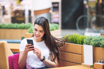 Young adult beautiful brunette girl happy sitting in cafe with mobile phone