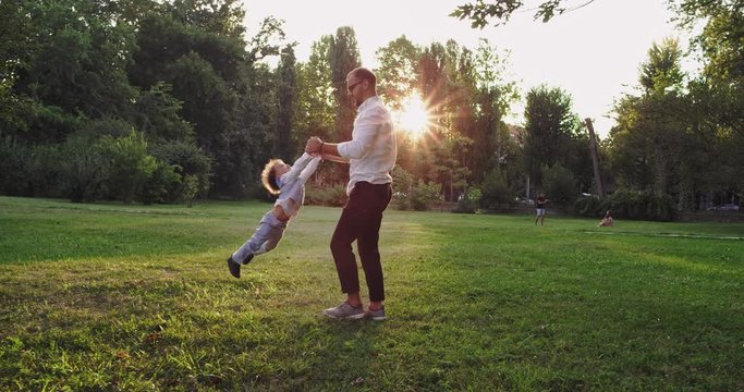 Smiling and happy dad playing lovely with his small son in the middle of the park at sunset enjoying the moment together