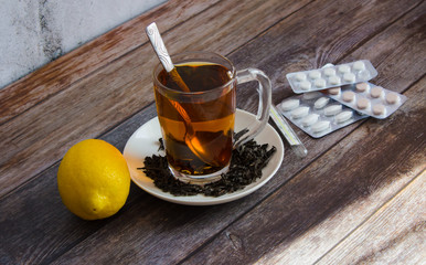 Tea with tea leaves, lemon, pills and thermometer on the background