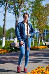 Beautiful girl in a denim jacket sits on a bench in a summer park