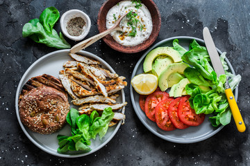 Grilled turkey, wholegrain bun, avocado, tomatoes, green salad and greek yogurt mustard sauce - ingredients for cooking hamburger on a dark background, top view