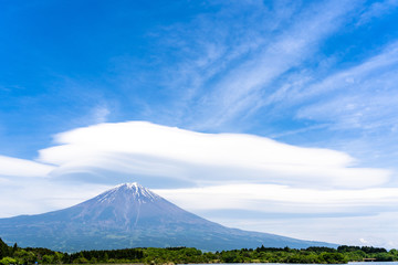 Fototapeta premium Fuji mountain with cloudy hat on top , fantastic clouds blue sky background spot view at Lake Tanuki (Tanuki-ko) in morning time near small hill and green forest foreground, Fujinomiya Shizuoka Japan.