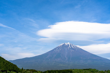Naklejka na ściany i meble Fuji mountain with cloudy hat on top , amazing clouds on blue sky background spot view at Lake Tanuki (Tanuki-ko) in morning time near small hill and green forest foreground ,Mount Fuji , Fujinomiya,