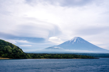Fuji mountain with cloudy hat on top , amazing clouds on blue sky background spot view at Lake Tanuki (Tanuki-ko) in morning time near small hill and green forest foreground ,Mount Fuji , Fujinomiya,