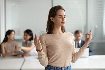 Mindful young businesswoman meditating, doing yoga exercise in office