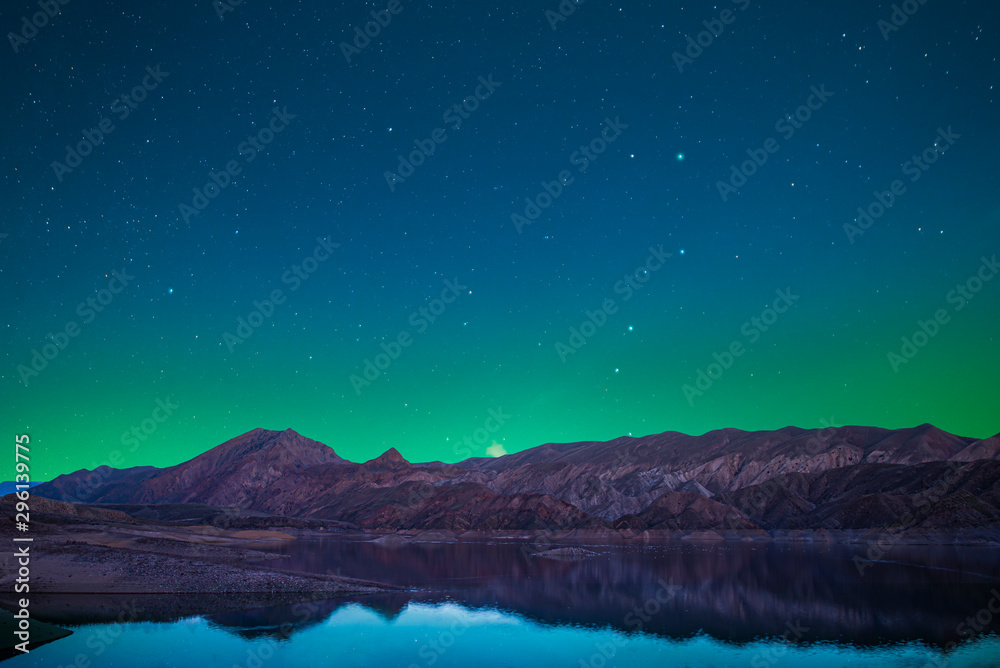 Wall mural beautiful lake and mountains in the starry night with green light over the mountains. night landscap