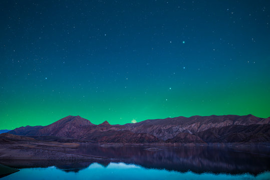 Beautiful lake and mountains in the starry night with green light over the mountains. Night landscape. 