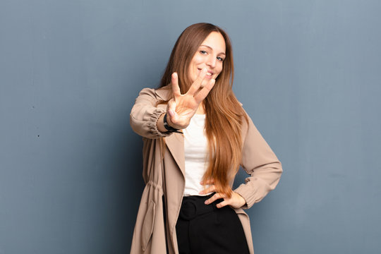 young pretty woman smiling and looking friendly, showing number three or third with hand forward, counting down against gray background