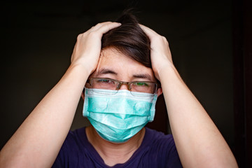 Ill Asian man with eyeglasses wearing hygienic mask feeling headache