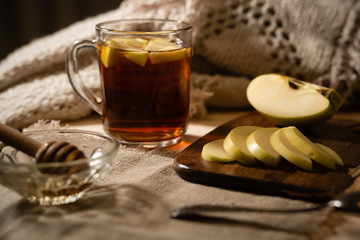 Black tea with apple slices in a glass cup. A slice of green apple on a blue plate. Wooden spoon...