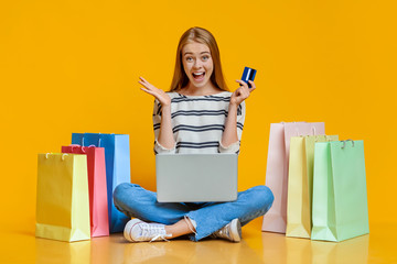 Girl holding laptop and credit card, sitting with shopping bags
