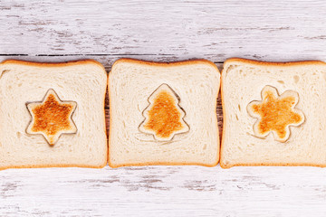 Slices of toast bread with a toasted cut out shaped like a fir-tree, star and snowflake on a wooden...