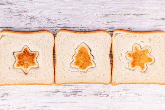 Slices of toast bread with a toasted cut out shaped like a fir-tree, star and snowflake on a wooden white background. Concept of Christmas morning breakfast meal.