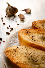 Croutons with black pepper in the corner of the photo on a white wooden surface. Garlic and black peas in the background are blurred. Vertical orientation.