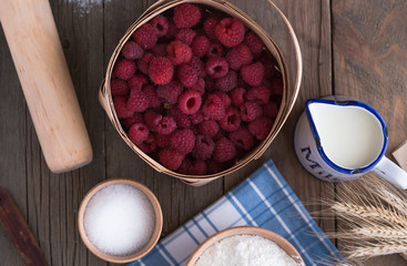 Baking cake in rural kitchen - dough recipe ingredients (raspberry, eggs, flour, milk, butter, sugar) and rolling pin on vintage wood table from above. Rustic background with free text space.
