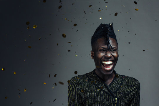 Portrait of an excited, happy young man laughing and celebrating, with gold confetti falling