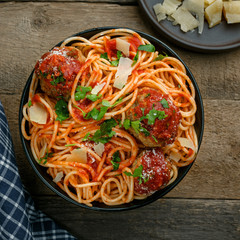 Traditional Italian spaghetti with meatballs and parmesan in tomato sauce in a black bowl. American family meal on a table. Top view shot.