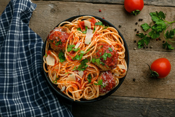 Traditional Italian spaghetti with meatballs and parmesan in tomato sauce in a black bowl. American family meal on a table. Top view shot.