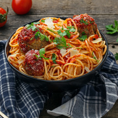 Pasta with meatballs, parmesan and tomato sauce in a clay bowl. Homemade Italian spaghetti on a rustic wooden table.