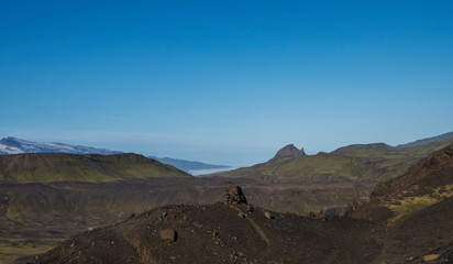 Icelandic lava desert landscape at Laugavegur hiking trail with stone boulders and view on Einhyrningur unicorn mountain. Fjallabak Nature Reserve, Iceland. Summer blue sky