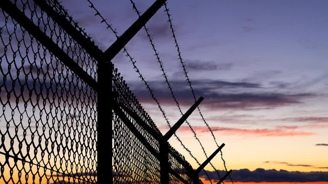 Wired Fence with Barbed Wire and Mesh Steel Wall at Twilight, Concept of Prison, Salvation, Refugee, Isolation,  Loneliness