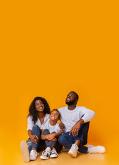Cheerful black family sitting on floor and looking upwards