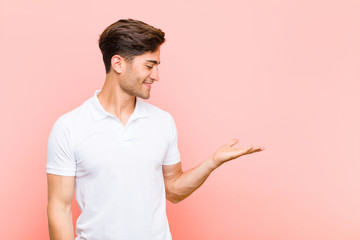 young handsome man feeling happy and smiling casually, looking to an object or concept held on the...