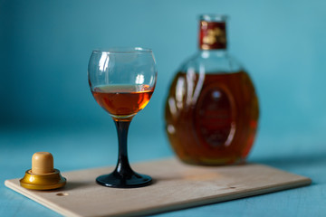 glass of cognac, bottle and cork on a wooden tray on a blue background