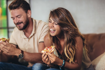 Couple eating pizza in modern cafe. They are laughing and eating pizza and having a great time.
