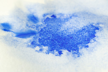 A stain of blue watercolor paint on paper dipped in water. Macro photo. Background minimalistic vibrant image. The concept of drawing...