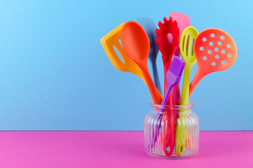 bright multi colored kitchen utensils on blue and purple background with copy space