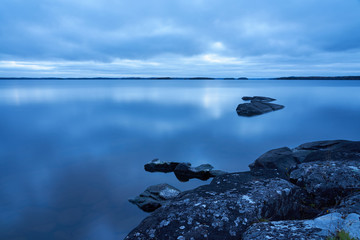                 Rocks on a foggy lake on twilight with rocky coast with moss on a foregroud. Copy space.               