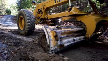 Closeup of scraper scraping dirt from road surface.
