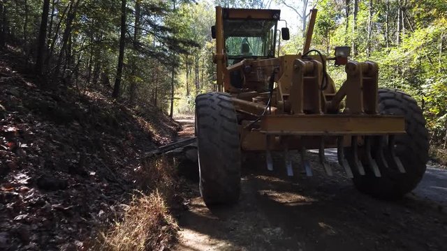 Road grader shot of front as it digs the dirt out of a culvert on the side of a road.