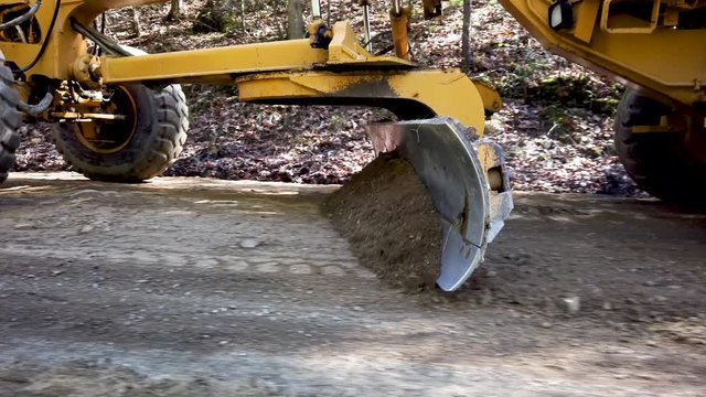 Closeup side shot of road grader scraper, scraping dirt for making a road.