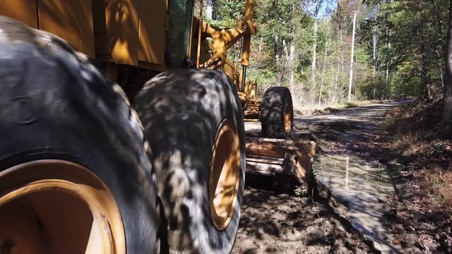 Closeup of industrial road grader from behind tire scraping dirt on construction of new roads.