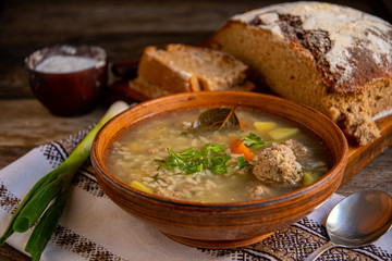 Soup with meatballs in a clay ceramic bowl, folk folk napkin on an old wooden table.