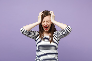 Frustrated crying young brunette woman girl in casual striped clothes posing isolated on violet purple background studio portrait. People lifestyle concept. Mock up copy space. Putting hands on head.