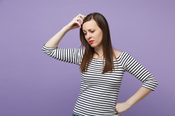 Fototapeta premium Preoccupied young brunette woman in casual striped clothes posing isolated on violet purple background studio portrait. People lifestyle concept. Mock up copy space. Looking down putting hand on head.