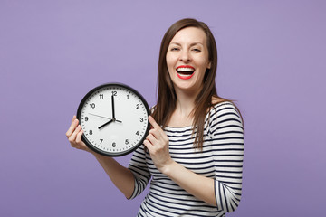 Young brunette woman girl in casual striped clothes posing isolated on violet purple background studio portrait. People sincere emotions lifestyle concept. Mock up copy space. Hold in hand round clock