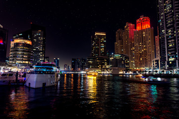 Fototapeta premium Dubai Marina at night with light reflections on the water, starry sky and a dhow cruise