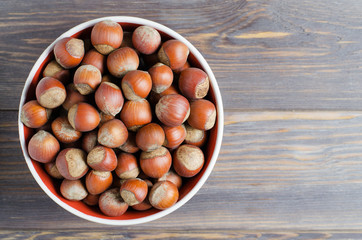 Obraz premium Hazelnuts in a white plate. Brown wooden background. Flat top view