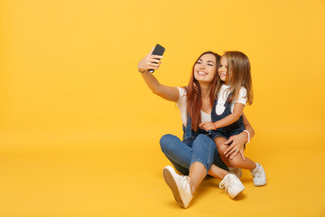 Woman in light clothes doing selfie with cute child baby girl 4-5 years old. Mommy little kid daughter isolated on yellow background studio portrait. Mother's Day family parenthood childhood concept.