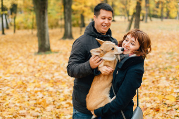 Naklejka na ściany i meble Happy couple playing with Corgi dog in sunny autumn park.