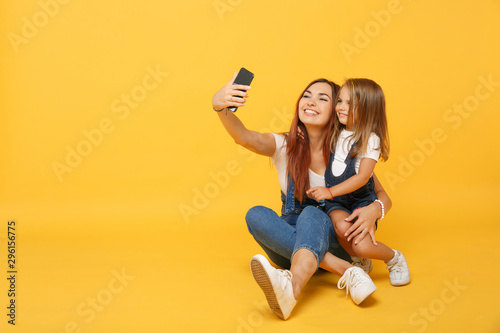 Woman in light clothes doing selfie with cute child baby girl 4-5 years old. Mommy little kid daughter isolated on yellow background studio portrait. Mother's Day family parenthood childhood concept.