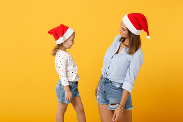 Obraz premium Woman child baby girl 4-5 years old in Christmas Santa hat. Mommy little kid daughter isolated on yellow background studio portrait. Happy New Year 2020 celebration holiday concept. Mock up copy space